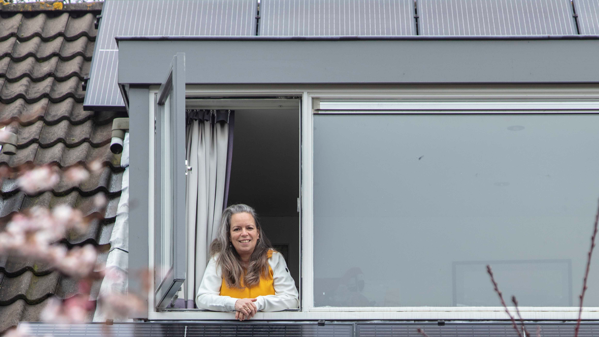 Foto van iemand die uit het raam kijkt met zonnepanelen op het dak (gemaakt door Henk Knoester)